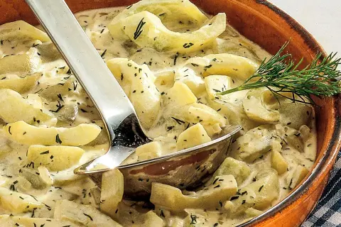 Cremige geschmorte Gurken mit Dill in einer Terrine, serviert mit einer Schöpfkelle.
