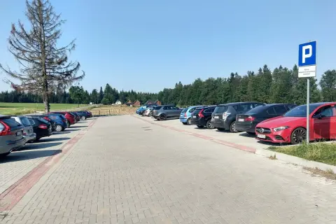 Parking przy górze Jagodnej. Samochody zaparkowane na utwardzonym placu, w tle las i domki.