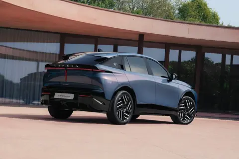 Lancia Gamma 2026, un'elegante berlina blu metallizzato con fari posteriori a LED, parcheggiata davanti a un edificio moderno.