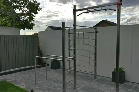 Eine Klimmzugstange für draußen mit Kletternetz und Barren im Garten. Perfekt für ein Outdoor-Workout.
