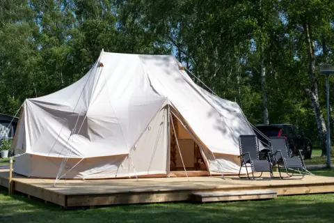 Stor glampingtält i Mölle med träaltan och solstolar. En bil syns i bakgrunden.