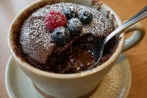 En kladdkaka i micro, toppad med bär och pudrat socker. En sked är nedsatt i den rinnande chokladen.