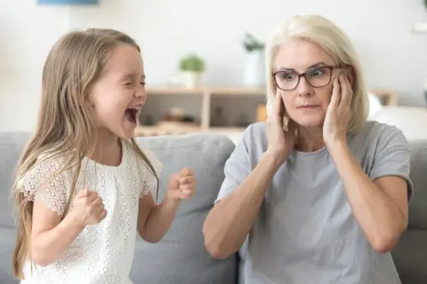 Rozkrzyczane dziecko nie może usiedzieć w miejscu, a babcia zakrywa uszy, próbując zapanować nad chaosem.