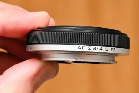 A hand holds a compact, black and silver pancake lens, labeled "AF 28/4.5 FE".