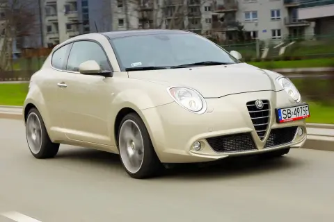 Złoty Alfa Romeo MiTo w ruchu miejskim. Wiele osób chwali ten model za wygląd, co potwierdzają alfa romeo mito opinie.