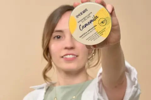 Mujer sonriente sostiene un desmaquillante en crema, "Camomila", que es un sebo limpiador con manteca de karité.