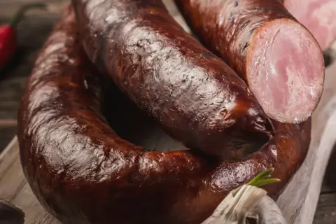Aromaticzna kiełbasa lisiecka, wędzona i rumiana, z widocznym przekrojem ukazującym soczyste mięso. Obok czosnek i papryczka chili.