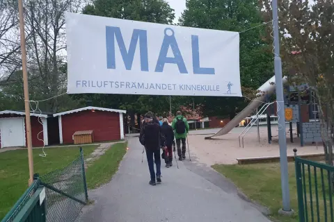 A banner reading "MÅL FRILUFTSFRÄMJANDET KINNEKULLE" hangs over a path where people walk towards a playground.