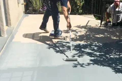 Peinture carrelage extérieur avant après : un homme peint une terrasse grise avec un rouleau, transformant l'espace.