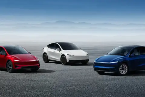 Trzy samochody Tesla: czerwony, biały i niebieski, stoją na pustkowiu.