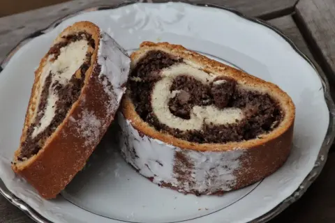 Dwa kawałki makowca, który zawsze się udaje, na białym talerzu. Ciasto jest puszyste, z widocznym nadzieniem makowym i kremowym.