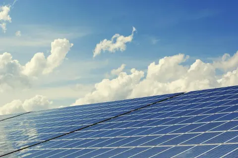 Paneles solares bajo un cielo azul con nubes. El sol brilla, pero la sombra de un posible impuesto al sol en España se cierne sobre la energía renovable.