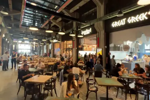Tętniący życiem food hall w Gdańsku. Ludzie siedzą przy stołach, jedzą i rozmawiają. W tle widać lokal "Great Greek".