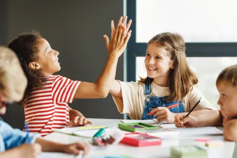 Kinder geben sich beim Lernen die Hand. Sie arbeiten an ihren Aufgaben, was gute Gruppenarbeit Methoden zeigt.