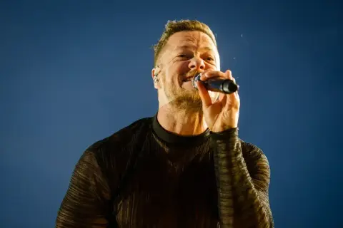 Wokalista Imagine Dragons śpiewa do mikrofonu na tle błękitnego nieba.