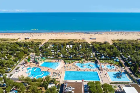 Widok z lotu ptaka na plażę i kompleks basenów w **marina do Venezia**. Widać morze, piaszczystą plażę z leżakami, camping i zjeżdżalnie wodne.