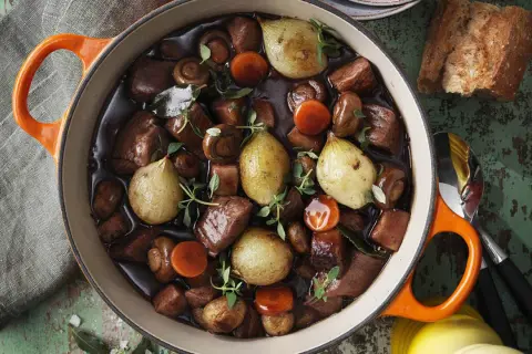 En mustig skinkstek i gryta med hela champinjoner, små lökar och morötter, garnerad med färsk timjan. Perfekt för en mysig middag.