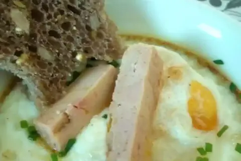 Œuf cocotte au foie gras, servi avec une tranche de pain aux céréales et des herbes fraîches. Un délice pour le palais.