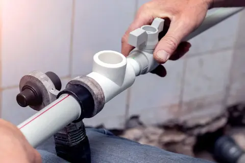 Instalator pokazuje, jak łączyć rury plastikowe do wody, montując trójnik.