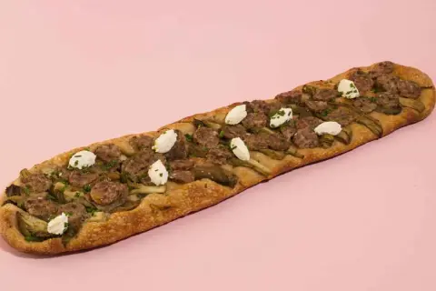 Deliciosa coca de recapte con salchicha, alcachofas y queso de cabra, lista para compartir.