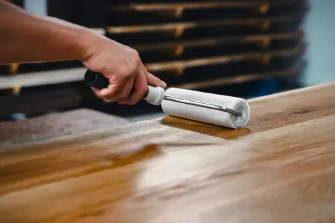 Main d'artisan appliquant un vernis sur un plateau en bois avec un rouleau, étape clé pour savoir comment vitrifier une table en bois.