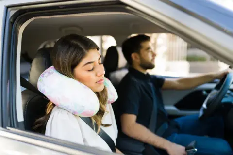 Donna dorme in auto con un cuscino cervicale fai da te, mentre l'uomo guida.