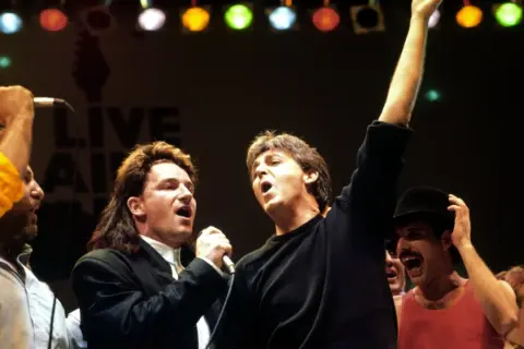 Bono und Paul McCartney singen bei Live Aid. Freddie Mercury jubelt im Hintergrund. Legendäre Live Aid Bands vereint.