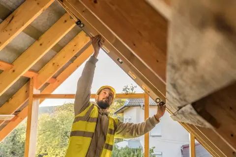Operaio con livella controlla la pendenza di un tetto a due falde in legno.