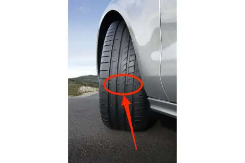 Neumáticos desgastados en un coche plateado en una carretera. La banda de rodadura muestra un desgaste desigual, indicando la necesidad de reemplazo.