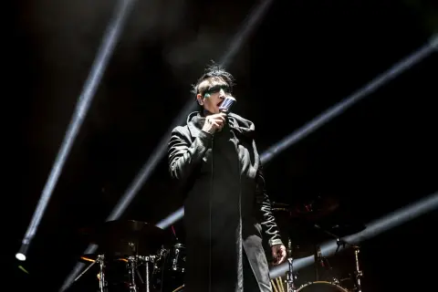 Marilyn Manson na scenie w Warszawie, w czarnym płaszczu i z charakterystycznym makijażem, śpiewa do mikrofonu.