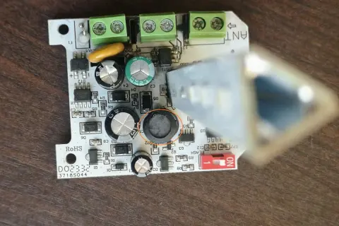 Uszkodzona lampa ostrzegawcza bramy. Widoczny element elektroniczny z okrągłym, czarnym uszkodzeniem.