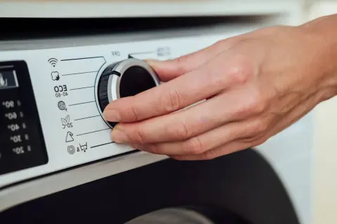 Dłoń kręci pokrętłem pralki Whirlpool. Rozwiązywanie problemów z instrukcją obsługi.
