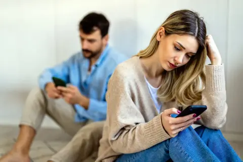 Een vrouw en man zitten apart, beiden op hun telefoon. Ze voelen zich leeg in hun relatie, de afstand tussen hen is voelbaar.