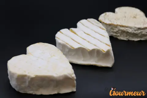 Trois fromages Neufchâtel en forme de cœur, dont un avec des stries, sur fond noir.