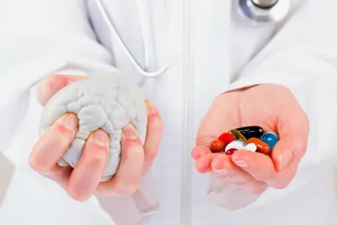Mains tenant un cerveau en plastique et une poignée de pilules colorées, symbolisant la recherche sur la maladie de Parkinson, dernière découverte.