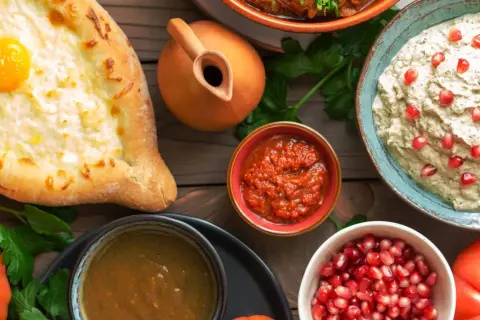 Gruzińska uczta: chaczapuri z jajkiem, sosy, bakłażan z granatem i pomidory. Najpiękniejsze toasty gruzińskie na drewnianym stole.