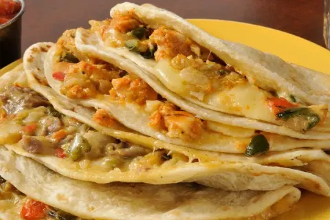 Quesadillas de pollo apiladas, rellenas de queso derretido y trozos de pollo sazonado, servidas en un plato amarillo con salsa al lado.