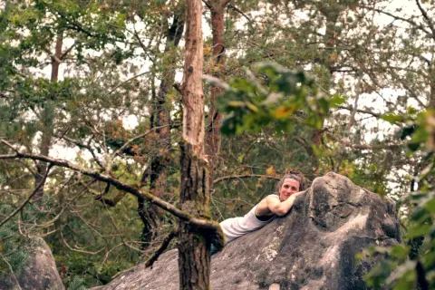 Frau ruht auf einem großen Fontainebleau Boulder im Wald, umgeben von Bäumen.