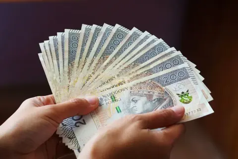 Dłonie trzymają wachlarz banknotów 200 zł. Pieniądze symbolizują świadczenie wspierające, które trafi do potrzebujących.