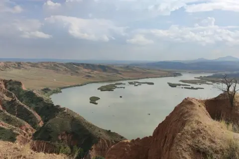 Paisaje de barrancos ocres y un lago sereno, ideal para una ruta de senderismo.