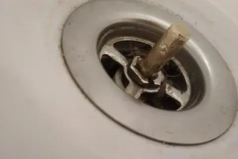 W umywalce widać wciśnięty korek, wokół którego zebrały się włosy i brud.