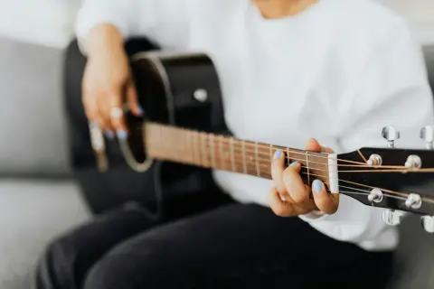 Dłoń z niebieskim lakierem na paznokciach gra na czarnej gitarze, tworząc rytmy w stylu reggae.