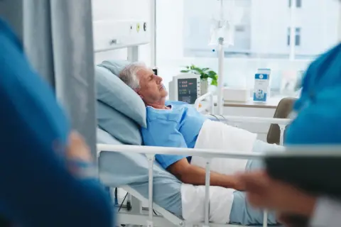 Starszy mężczyzna w szpitalnym łóżku, z kroplówką i monitorem, może mieć objawy hantawirusa.