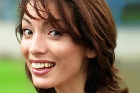 Close-up of a young woman with brown hair, smiling and looking to the side.