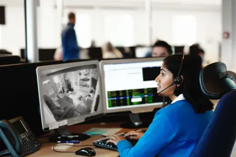 Kvinna med headset övervakar kameror på en arbetsplats, följer brandrutiner.