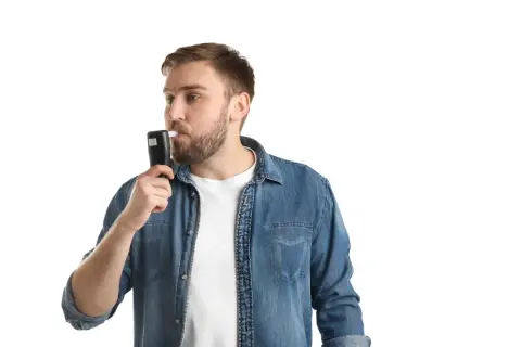 Mężczyzna w dżinsowej koszuli dmucha w alkomat. Czy można zbadać pracownika alkomatem? Tak, w określonych sytuacjach.