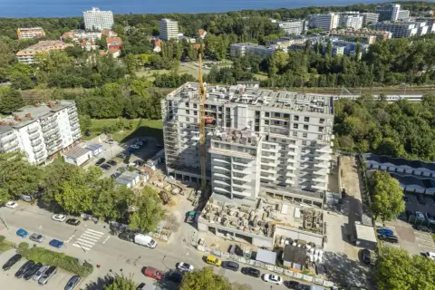 Budowa nowoczesnych, prywatnych mieszkań do wynajęcia nad morzem. Widok z lotu ptaka na osiedle w trakcie realizacji, z dźwigiem budowlanym i widokiem na morze w tle.