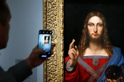 Osoba robi zdjęcie telefonem komórkowym obrazu "Salvator Mundi" przedstawiającego Jezusa.