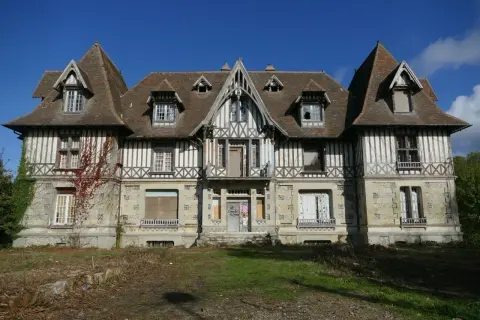 Maison abandonnée en Normandie, typique de l'urbex. Façade en colombage et pierre, toiture pentue, fenêtres brisées.