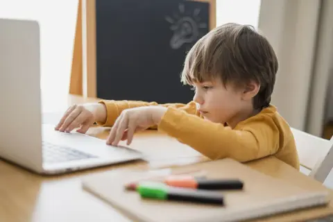 Chłopiec z problemami z koncentracją u dziecka siedzi przy laptopie, zamyślony. Na tablicy rysunek żarówki.